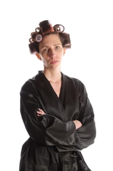 Adult housewife with curlers in her hair and a bathrobe stands against a white background and with a basket of ironing and an iron.