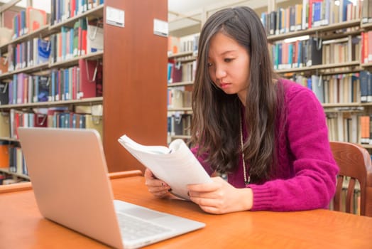 Woman with book and laptob studying in library