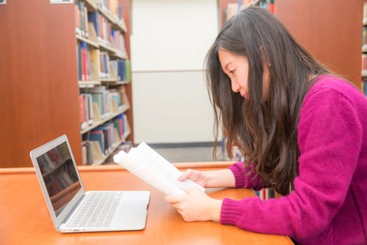 Woman with book and laptob studying in library