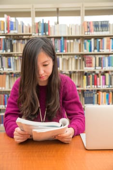 Woman with book and laptob studying in library