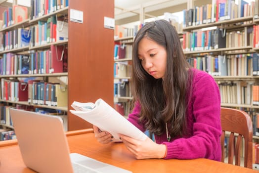 Woman with book and laptob studying in library