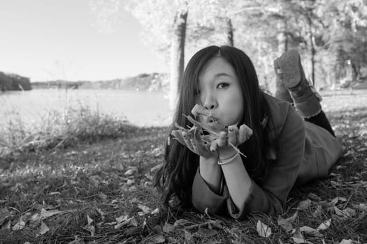 Woman laying on grass blowing away a handful of leaves
