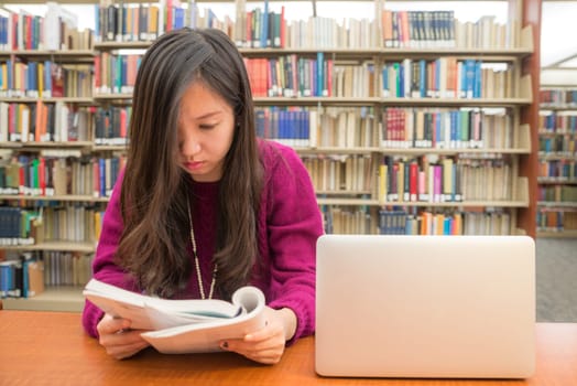 Woman with book and laptob studying in library