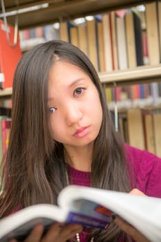 Woman reading a book next to a book shelf in library