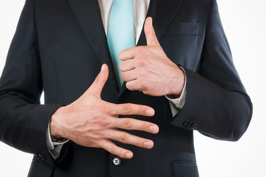 Chest-and-belly view of a young man in a black suit with his hands held in front of him indicating the "6"" (six fingers)"