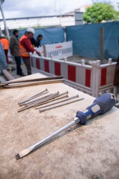 Wide-angle close-up of a screwdriver on a table with nails on a construction site with blurred and unrecognizable construction workers in the background in daylight