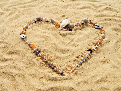 Heart from cockleshells and sea pebbles laid out on sand