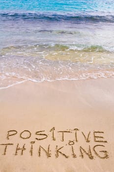 Positive Thinking message written on sand, with waves in background