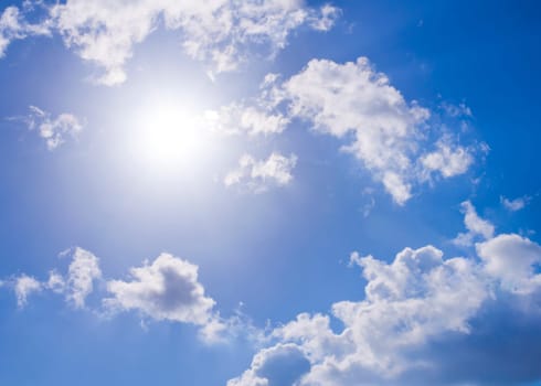 Sun against bright blue sky and white clouds