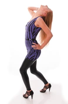 Attractive young woman with long blonde hair wears a blue mini dress with black glossy leggings and poses isolated against a white background.
