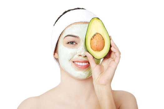 Young woman with a  smile holding avocado heaving face clay mask on the face in a spa