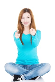 beautiful casual woman sitting pointing on camera. isolated on white.