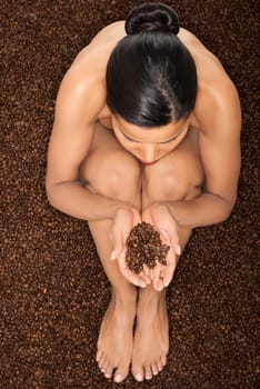 beautiful naked woman sitting in coffee seeds on them holding hands. up front view. closeup.