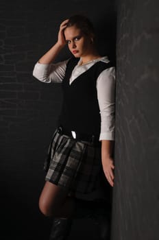 A young girl with blouse and boots stands in a dark corner of the room