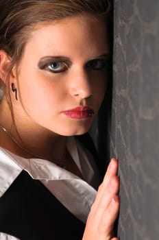 A young girl with blouse and boots stands in a dark corner of the room