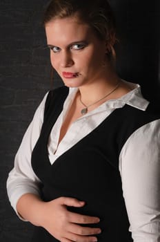 A young girl with blouse and boots stands in a dark corner of the room