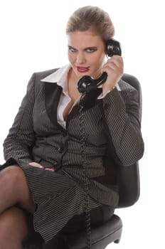 Young woman in grey business suit and high heels making calls with landline telephone against a white background