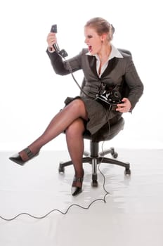 Young woman in grey business suit and high heels makes calls with landline telephone and yells angrily into the receiver against a white background