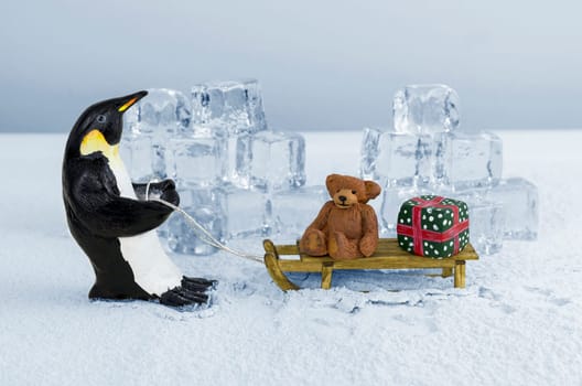 Penguin pulling sled with a teddy bear and a gift on board