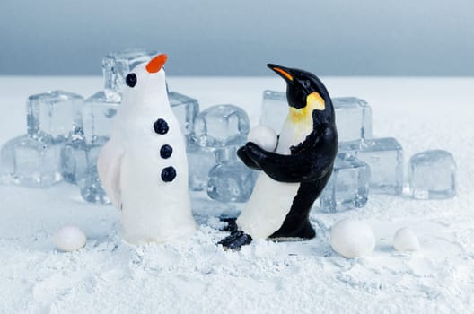Penguin lifting a snowball to make a snow penguin