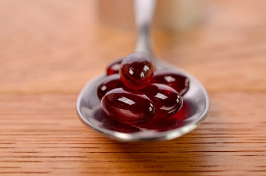 Red capsules on a spoon with a wooden background