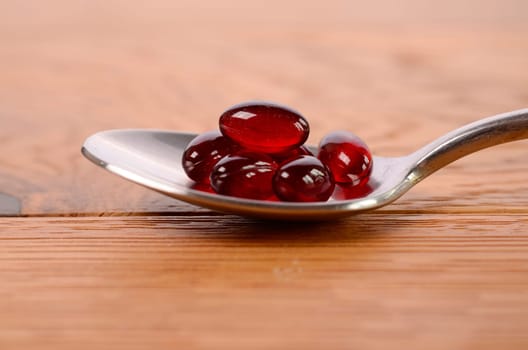 Red capsules on a spoon with a wooden background