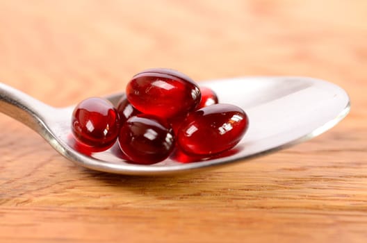 Red capsules on a spoon with a wooden background
