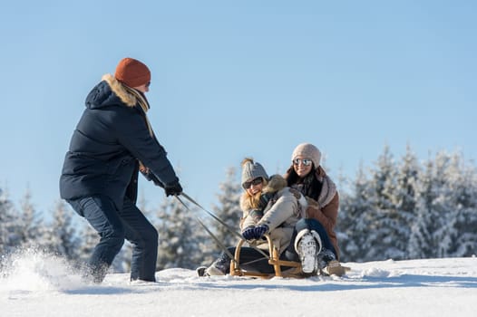 Young man pulling girls on winter sledge snow countryside