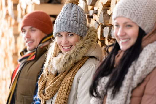 Three young people posing winter fashion leaning against wooden logs