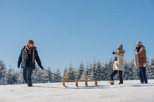 Young man pulling snow sledge winter countryside female girlfriends