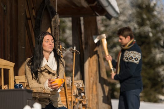 Young couple by snow winter cottage enjoying tea spending holiday