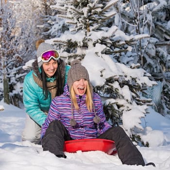 Two female friends on bobsleigh winter snow laughing having fun