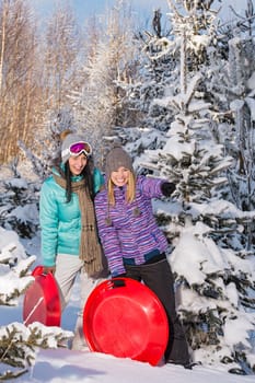 Two girlfriends in winter snowy forest with bobsleigh pointing