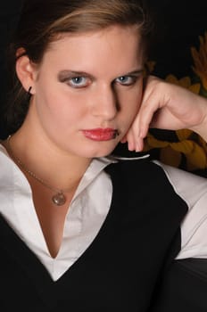 A young girl with a blouse and boots sits teasingly on a black leather armchair against a dark background