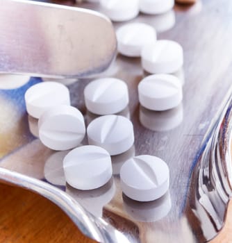 Close-up of two white medical pills on stainless steel tray.