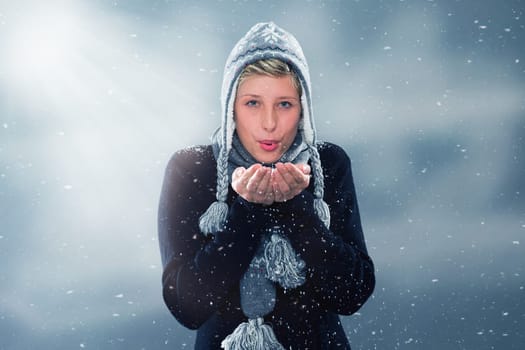 Young woman in the snowfall blows snow from her hands