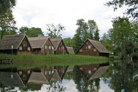 brown wooden boathouses reflecting in the water with reed and trees in the background