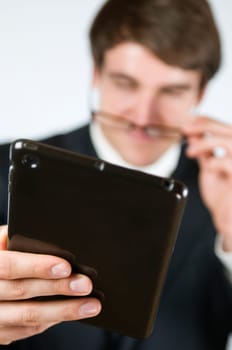 Upper body shot of a young man in a black suit and glasses against a white background,looking towards a tablet computer towards the camera  Head in the blurred background