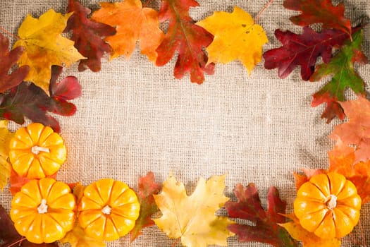Fall-themed background of burlap, dry leaves and pumpkins