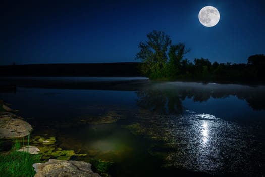 Scenic nighttime landscape with full moon rising over the lake