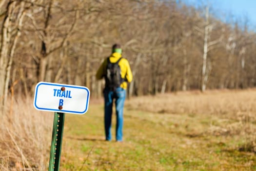 Image of a hiker on a trail with focus on the trail marker