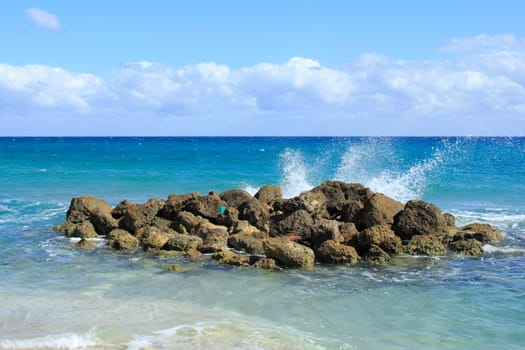 On a bright sunny day waves splash onto rocks on Deerfield Beach, Florida a beautiful scene and memorable because of it splendid beauty, unusualness and energy with its blue cloth washed ashore..