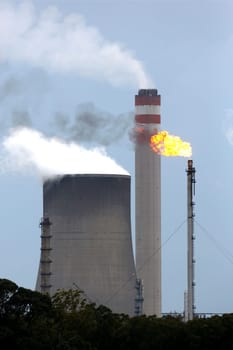Energy production plant with cooling towers, chimneys and gas flame