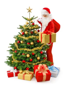 Santa Claus stands next to the Christmas tree and presents a gift box