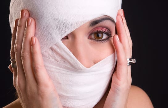 Woman in pain holds her head that has been injured and wrapped in first aid gauze