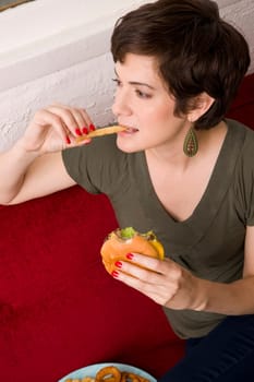 Woman eats french fries while holding a cheeseburger