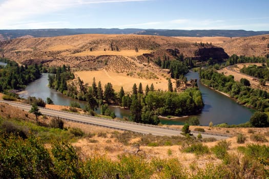 The road goes along next to a meandering river in the country