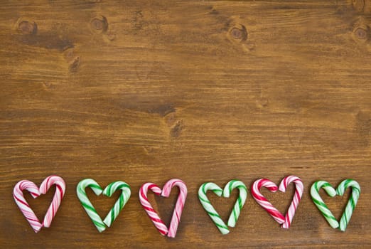 Colorful candy canes in heart shape on wooden background