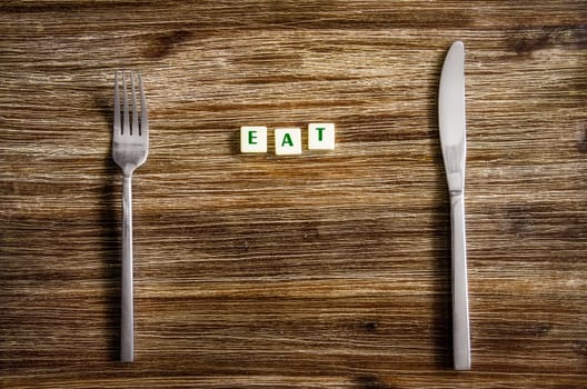 Knife and fork set on a wooden vintage table with sign Eat
