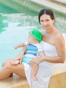 Baby and mother are sitting on the edge of a pool
